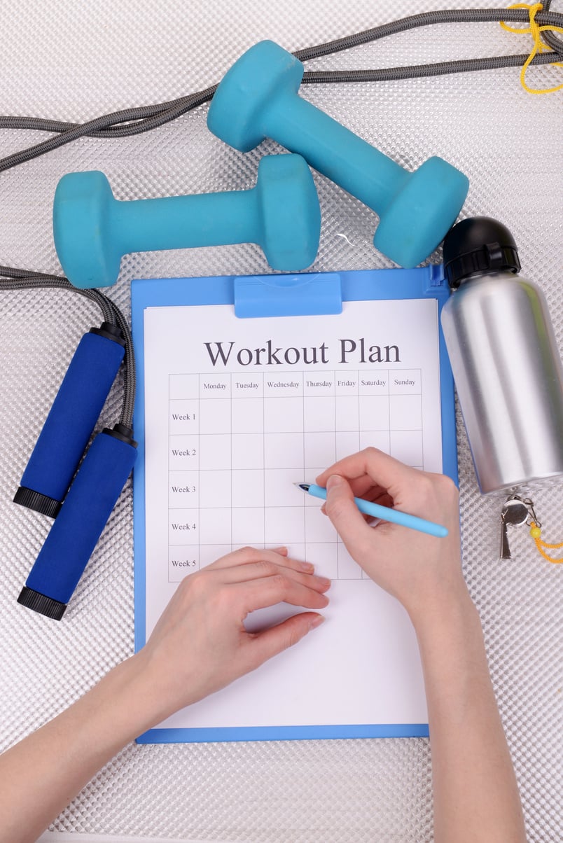 Image of a clipboard with a hand written workout plan, dumbbells and other fitness equipment.