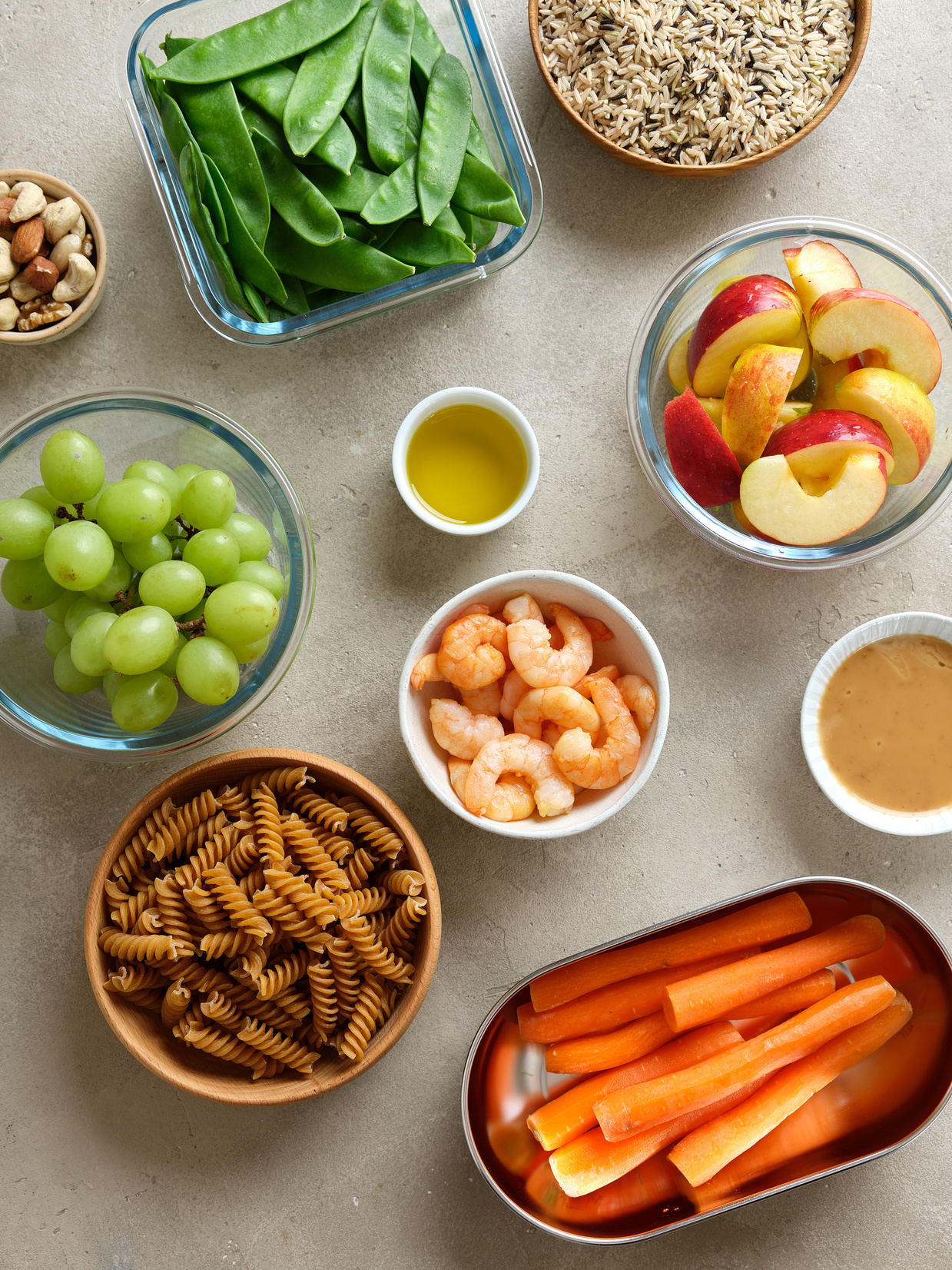 Image of several small bowls with vegetables, fruits, nuts, and other whole foods arranged on a table.